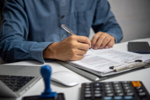 An image of a man holding a pen and filling out a form on a clipboard.