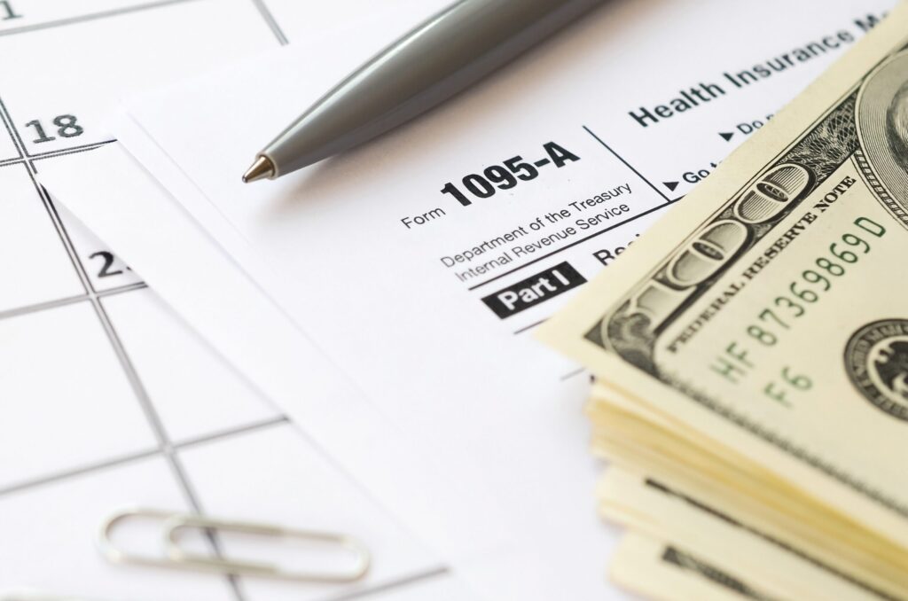 Image: A person sitting at a desk, surrounded by paperwork and a laptop, while holding a premium tax credit