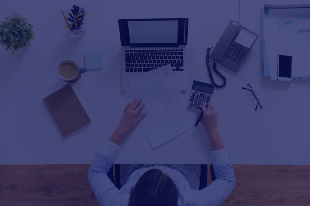 Image of a woman working on her desk with a laptop, paperwork and a cup of coffee.